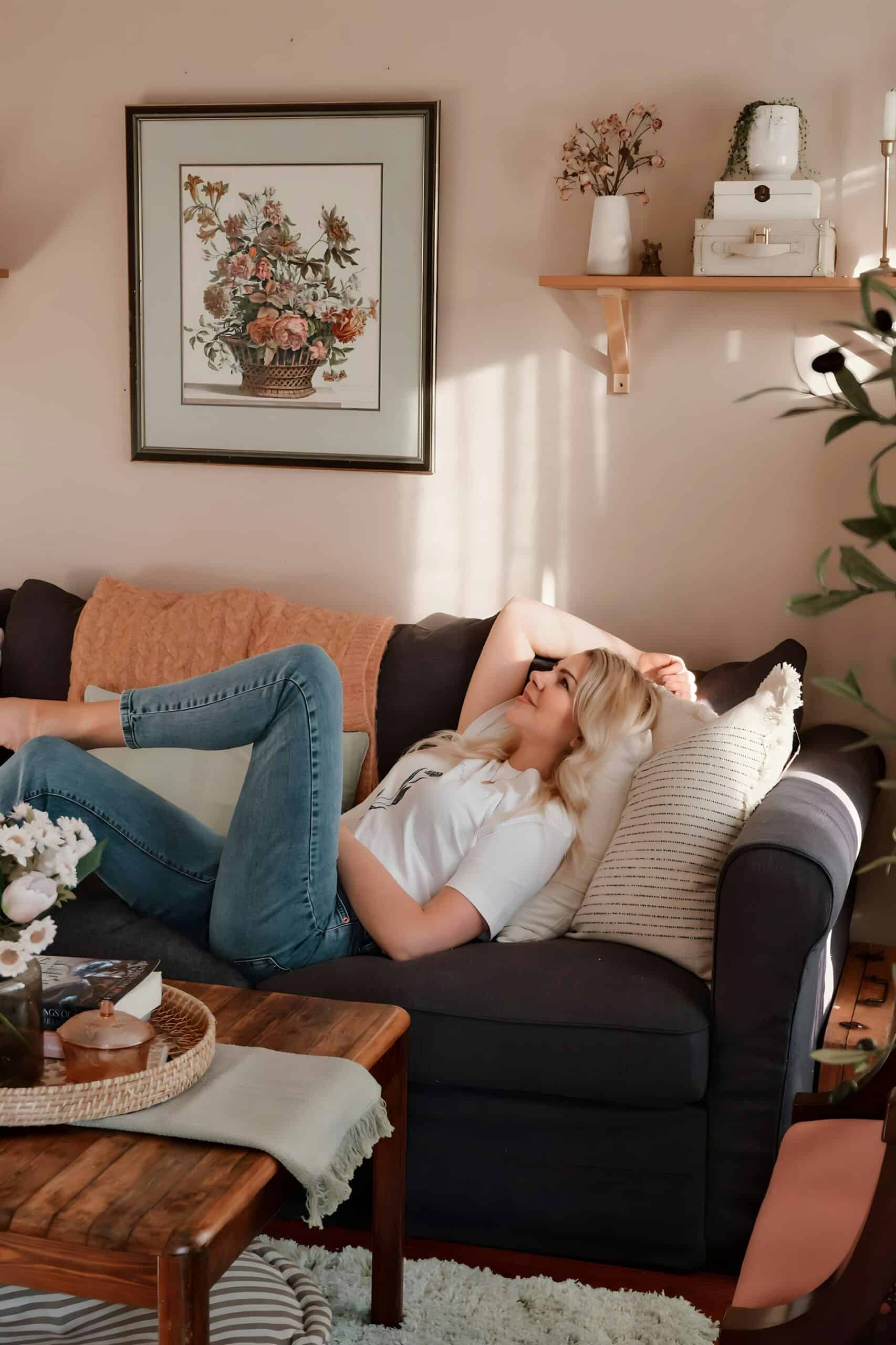 A woman relaxing on a cozy couch in the afternoon light, representing effortless, lazy girl self-care.