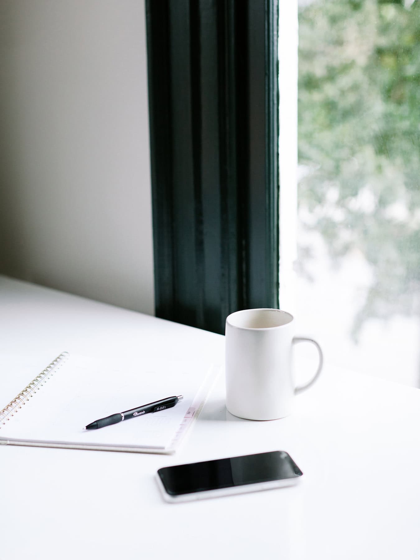 Minimalist desk with open planner, pen, white coffee mug, and smartphone by a window - showing how to plan your week without overload.