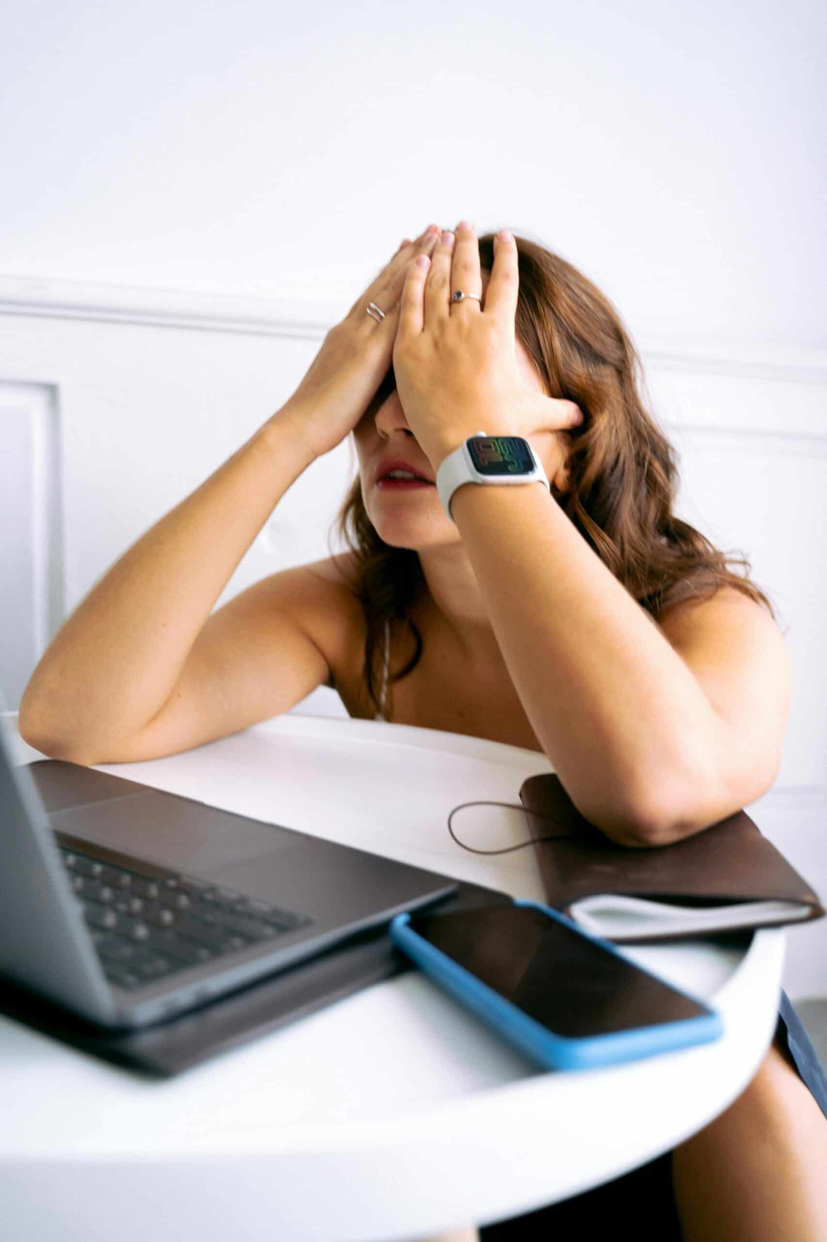A woman sitting at a desk with her head in her hands, looking overwhelmed and burned out — a visual representation of knowing it’s time to quit your job.