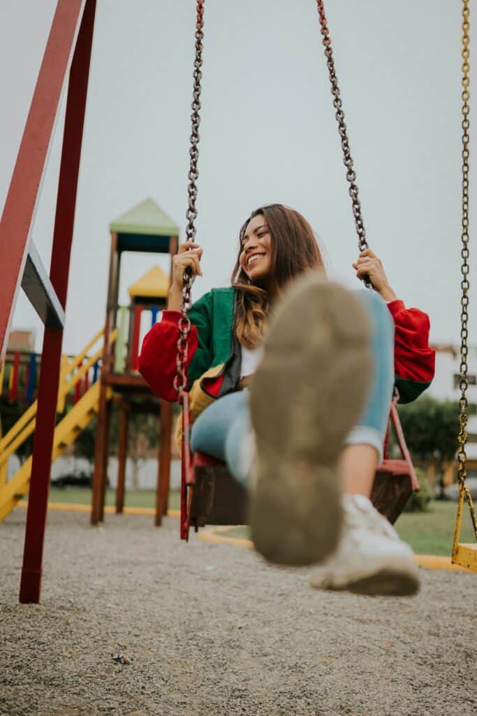 A woman laughing while swinging at a park, tapping into childhood joy as one of many ways to relax when stressed.