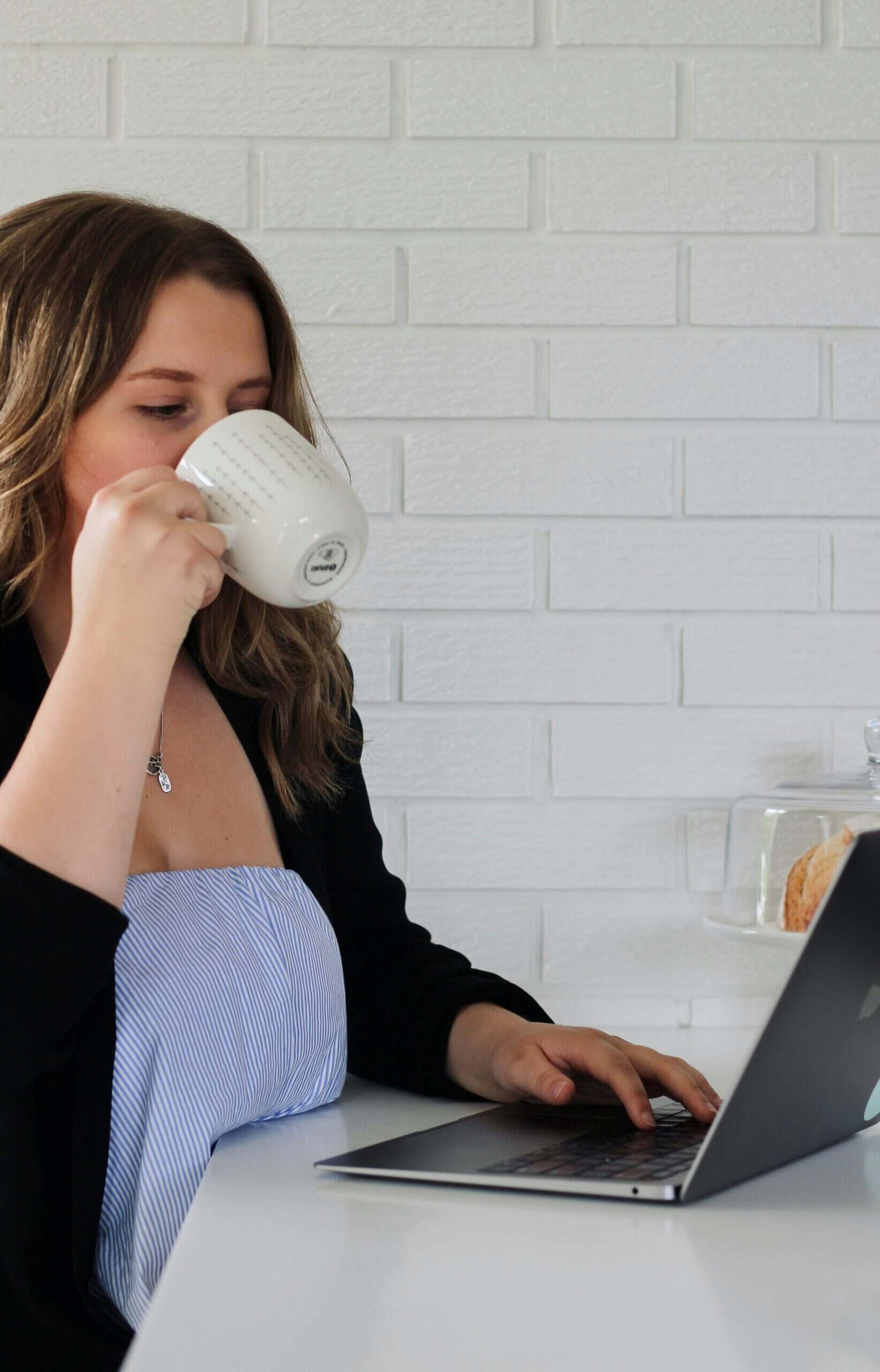 Woman drinking coffee while working on laptop — ADHD decision fatigue concept.