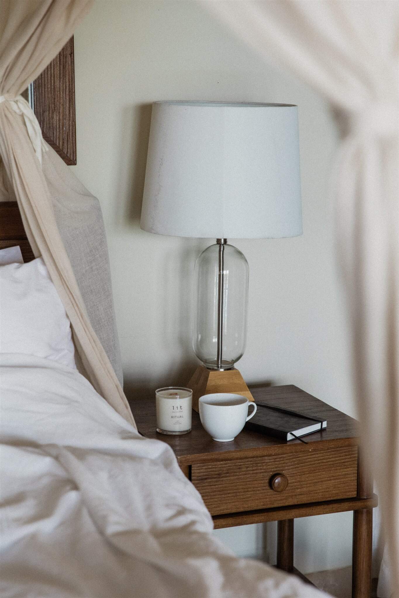 A cozy bedside table with a warm lamp, candle, mug, and journal, showing simple calming home tips for ADHD.