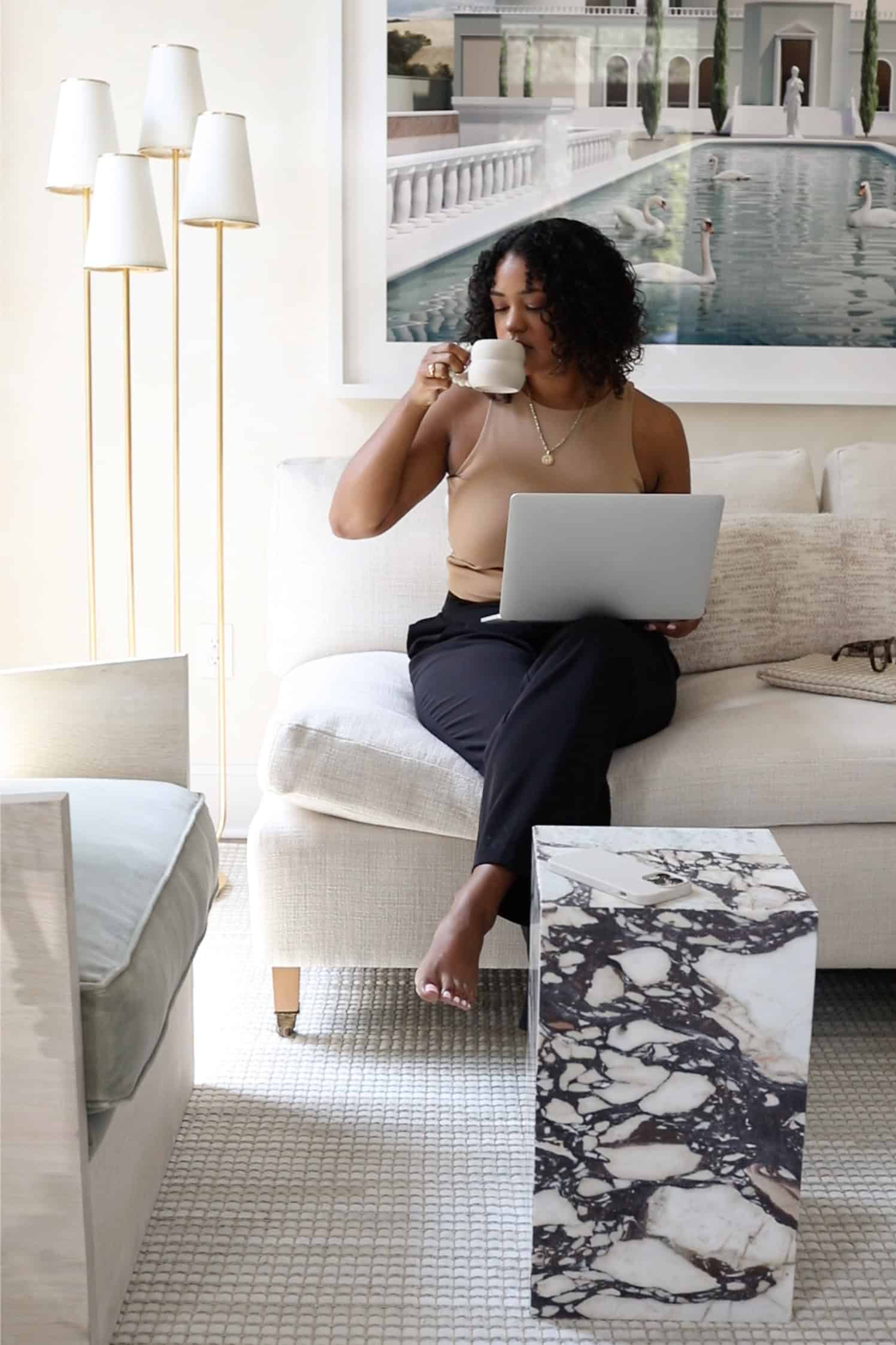 Woman sitting on couch with laptop and coffee, paused mid-task — showing how ADHD New Year goals can feel overwhelming and hard to start.