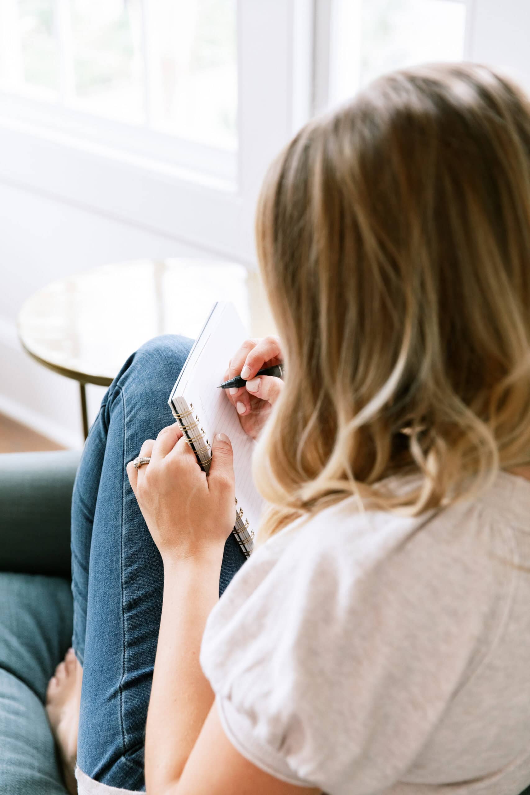 Woman sitting in a chair journaling, illustrating gentle personal growth habits focused on reflection and self-awareness.