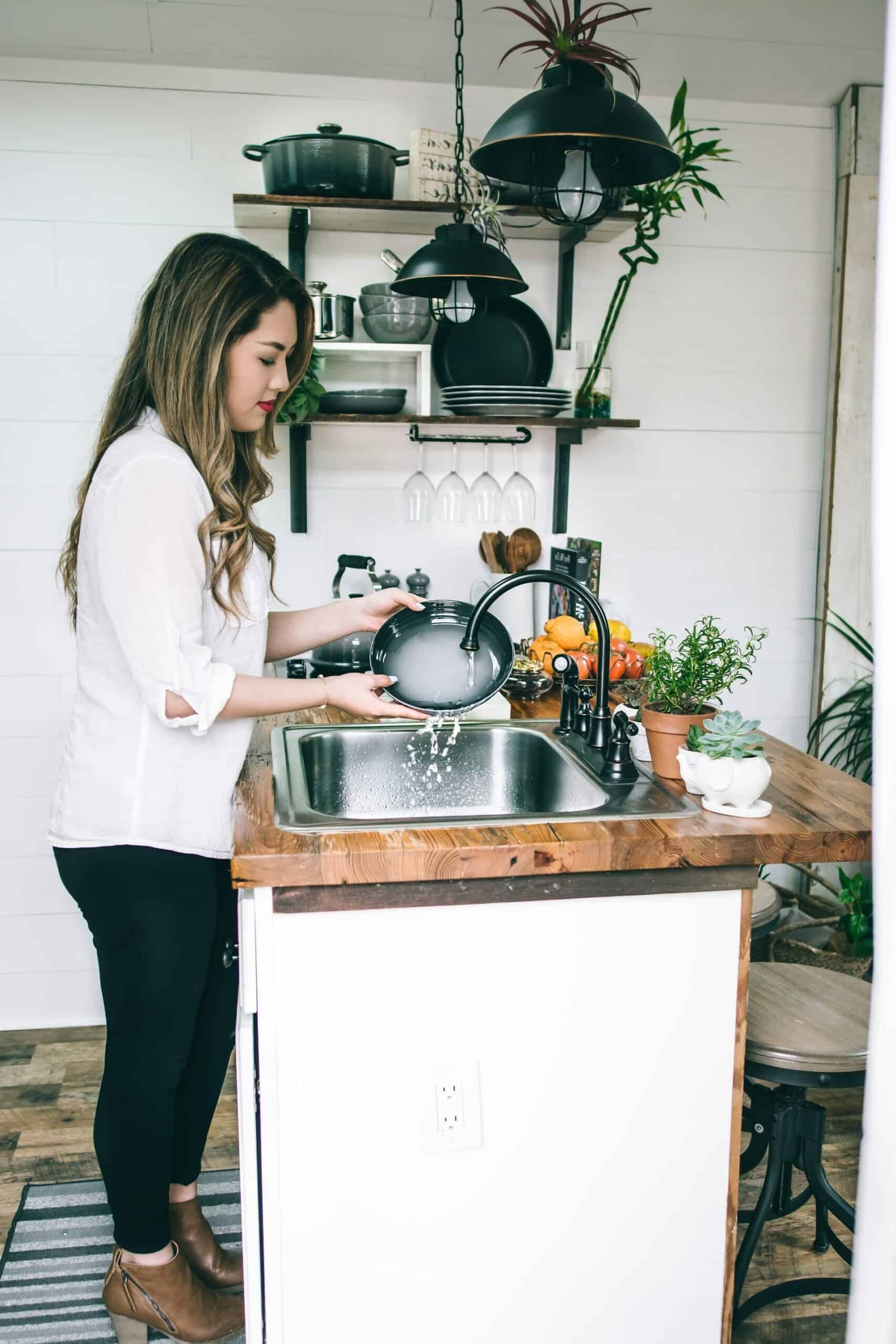Woman washing dishes at kitchen sink as part of realistic ways to clean with ADHD and reduce overwhelm.