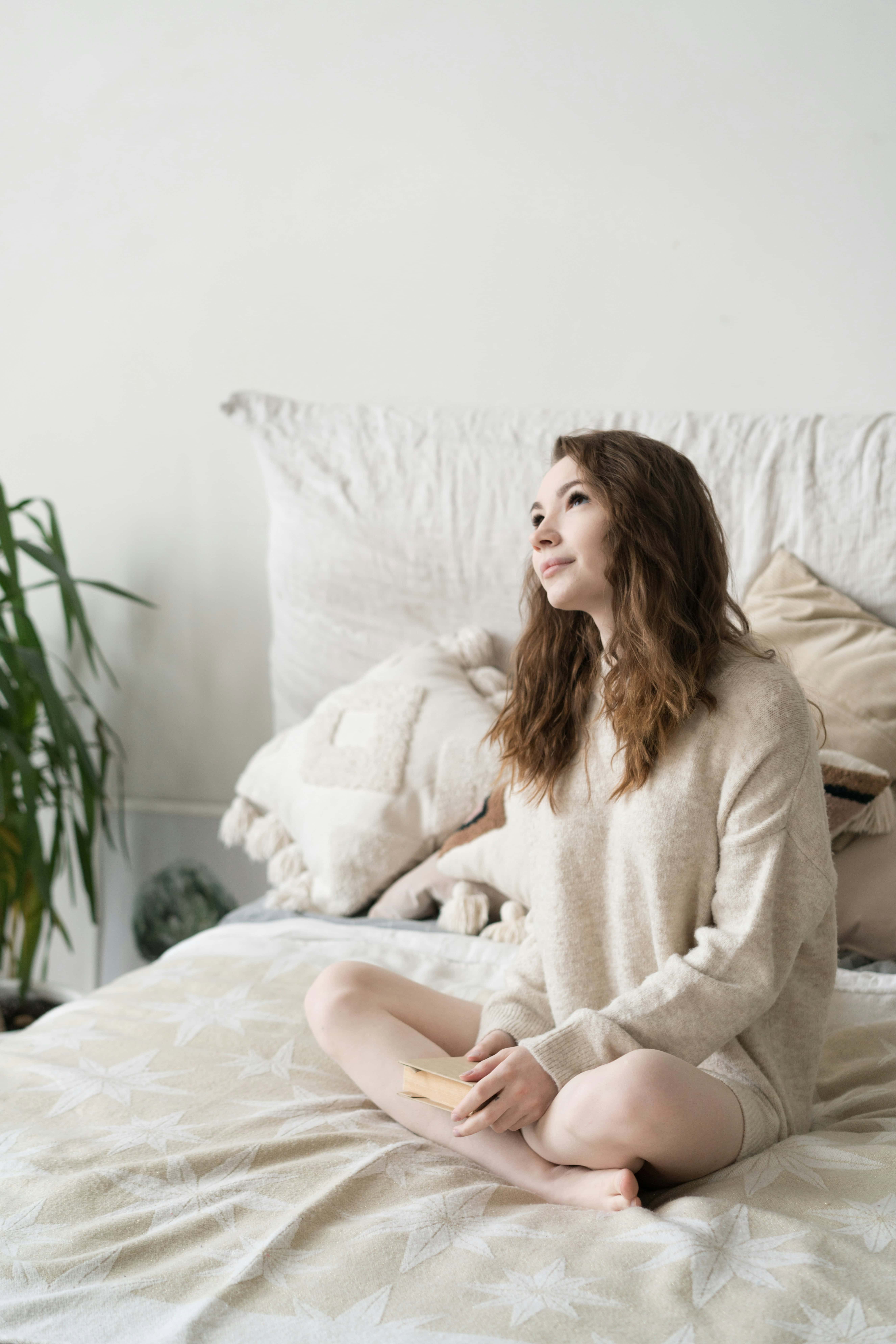 Woman sitting on bed in soft morning light looking thoughtful, representing common ADHD morning mistakes that make the day harder.
